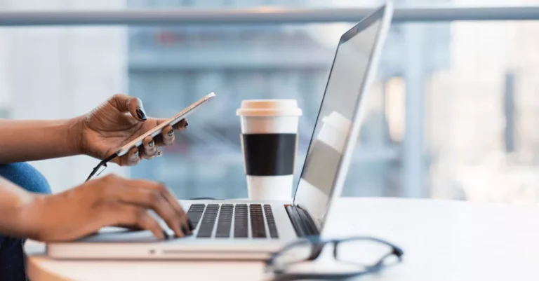 A person works on a laptop with a coffee