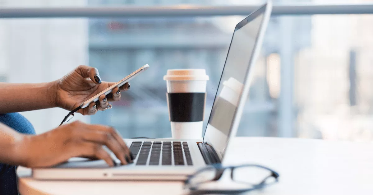 A person works on a laptop with a coffee