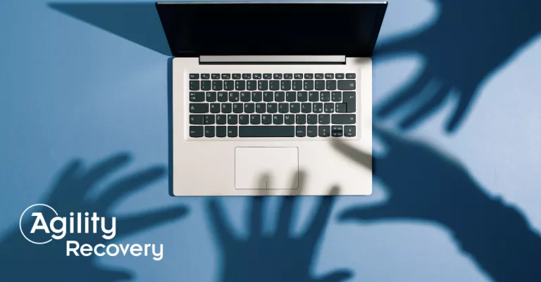 Shadowy hands over a laptop representing cyber crime and AI