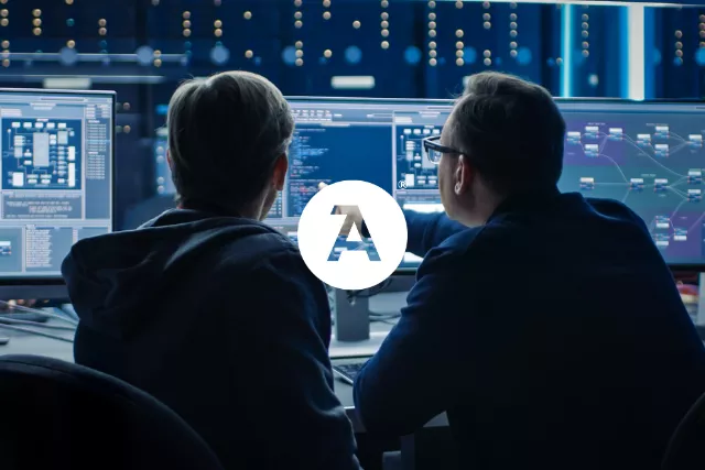 Two employees in front of several computers