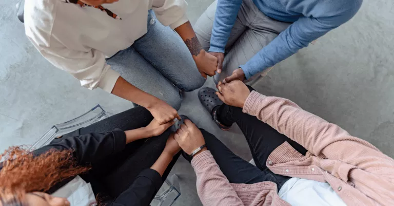 Business people sitting in a circle holding hands