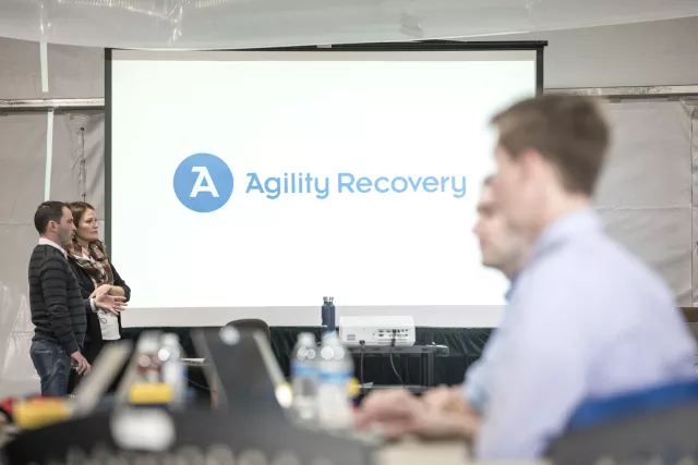 People sitting in an onsite offsite Workspace recovery with "Agility Recovery" on the projection screen